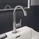Edelstahl-Waschtischarmatur mit hohem Auslauf und seitlichem Hebel, installiert auf einem weißen Waschbecken, vor schwarzer Fliesenwand, von Ideal Standard.